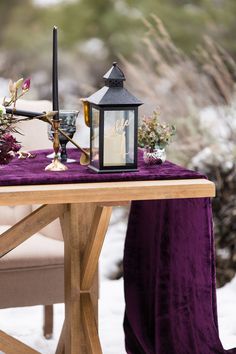 a table topped with a purple cloth covered tablecloth next to a small black lantern