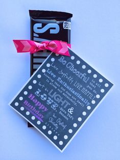 a candy bar wrapped in pink ribbon next to a black and white sign with happy birthday written on it