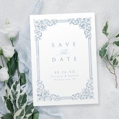 a wedding save the date card next to flowers and greenery on a white background