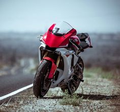 a red and white motorcycle parked on the side of a road next to a field