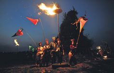 some people are standing around with flags and fire in the air at night, while one person is on an elephant