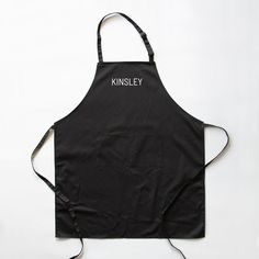 a black apron with the words kinsley on it, and an embroidered white line across the front