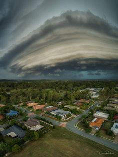 an aerial view of a storm moving through the sky over houses and trees in a suburban area