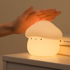 a person's hand reaching for a lamp that looks like a mushroom on top of a bookshelf