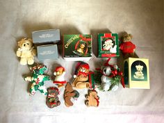 several small teddy bears and other christmas ornaments on a bed with white sheets, next to an empty box