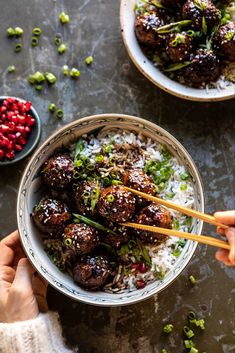 two hands holding chopsticks over rice with meatballs and garnishes