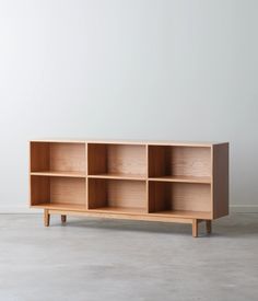 a wooden shelf with four compartments on one side and two legs, in front of a white wall