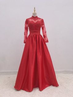 a red ball gown with long sleeves and lace on the top, in front of a white wall