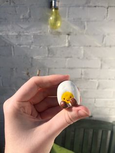 a person holding an egg with a smiley face on it in front of a brick wall