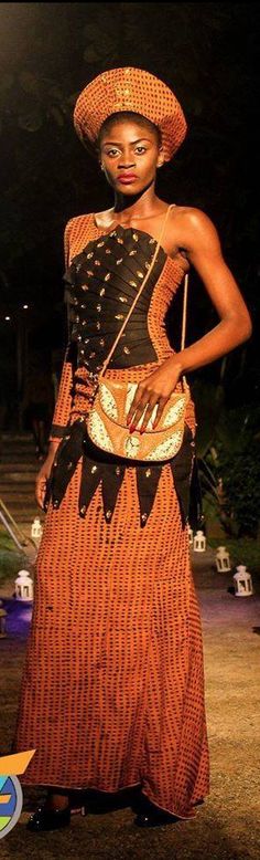 a woman in an orange and black dress with a hat on her head, holding a purse