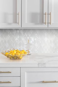 a bowl filled with lemons sitting on top of a counter next to white cabinets