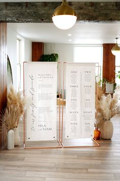 two tall white signs sitting on top of a wooden floor next to vases and plants