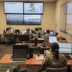 several soldiers are sitting at their desks in front of large screens and laptops