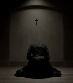 a woman in a black dress sitting on the floor with a cross above her head