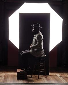 a man sitting on top of a stool in front of a white light that is behind him