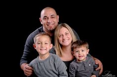 a woman and two boys are posing for a family photo in front of a black background