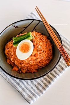 a bowl filled with noodles and an egg sitting on top of it next to chopsticks