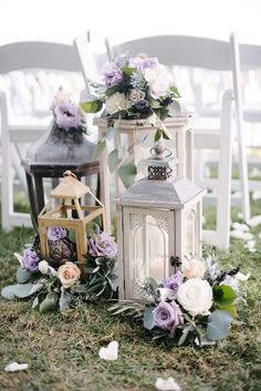 two white lanterns with flowers and greenery on the ground next to eachother