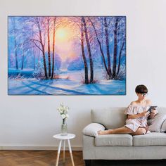 a woman is sitting on a couch in front of a painting that looks like a winter scene