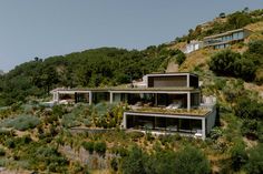 two houses on the side of a hill with trees and bushes growing on it's sides