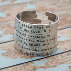 a stack of silver bracelets with words on them sitting on top of a wooden table