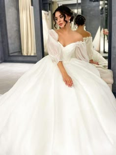 a woman in a white wedding dress sitting on a chair looking at herself in the mirror