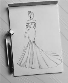 a drawing of a woman in a long dress on a piece of paper next to a pen