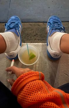 someone is sitting down with their feet on the edge of a table and drinking from a cup