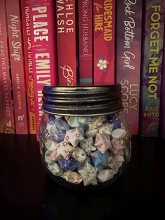 a glass jar filled with lots of candy next to some books on a black table