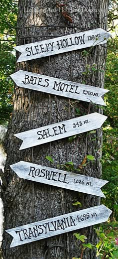 several signs on a tree pointing to different places in the woods, with names written on them