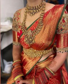 a woman in a red and gold sari with jewelry on her neck, sitting down