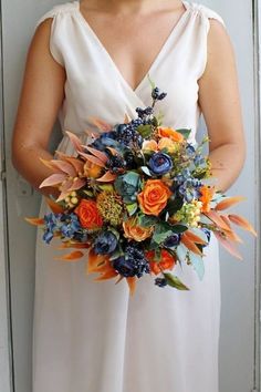 Add a pop of bold elegance to your wedding day with this stunning navy and burnt orange silk bouquet. Handcrafted with high-quality silk flowers, this bridal bouquet captures a rich autumn-inspired color palette perfect for rustic, boho, or outdoor weddings. The deep navy blues beautifully contrast with the warm orange tones, creating a striking and timeless arrangement that looks fresh all day long. Check out our picks for the best 5 navy blue November fall wedding color schemes November Wedding Colors Schemes, Color Schemes Wedding, November Wedding Colors, Fall Wedding Color Schemes, Purple Bouquets, Burnt Orange Weddings, Silk Bouquet, Outdoor Fall Wedding, Purple Wedding Flowers