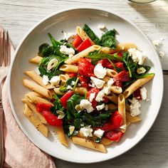 a white plate topped with pasta, spinach and feta cheese next to a fork