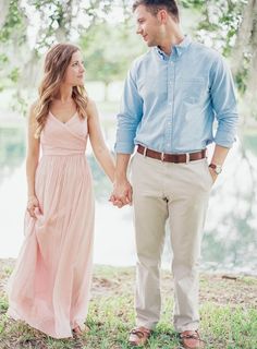 a man and woman holding hands while standing next to each other in front of water