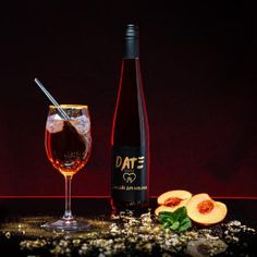 a bottle of wine sitting next to a glass filled with liquid and sliced peaches