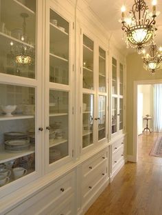 a white china cabinet with glass doors and chandelier hanging from it's ceiling