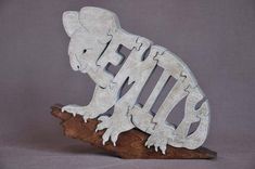 a metal gecko sitting on top of a piece of wood with the letter e in it