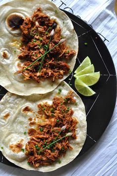 two tortillas with shredded meat and garnishes on a black plate