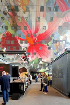 people are walking around in an indoor shopping mall with colorful ceiling tiles on the walls