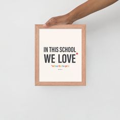 a person holding up a framed poster with the words in this school we love