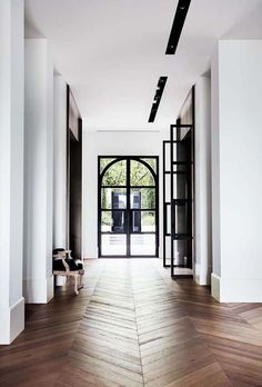 an empty hallway with wooden floors and black doors leading to another room that has large windows