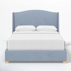 a bed with white pillows and blue headboard on top of it, against a white wall