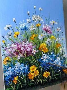 a painting of colorful flowers on a blue background is being held up by a person's hand