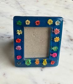 a blue frame with colorful flowers on it sitting on a marble counter top next to a white wall