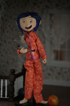 a doll with blue hair is holding a bird in her hand and standing next to an orange ball