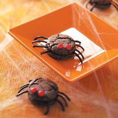 two chocolate spider cookies sitting on top of a orange plate next to another one with red eyes