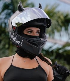 a woman wearing a helmet with horns on her face and gloves around her neck, standing in front of palm trees