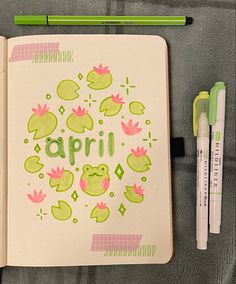 an open notebook with the word april written in green and pink on it next to two markers