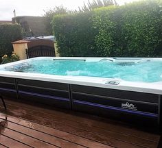 a hot tub sitting on top of a wooden deck next to a green hedge covered yard