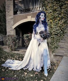 a woman with blue hair and makeup is dressed up as corpse from corpse in front of a building